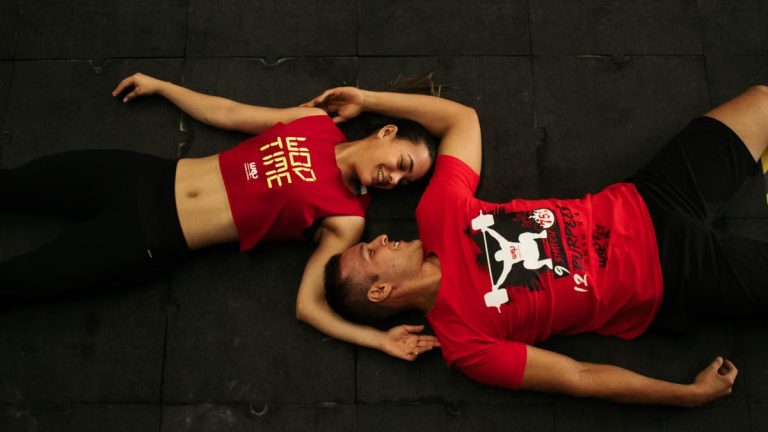 A man and woman relaxing on gym floor in Colombia, wearing matching red workout clothes.